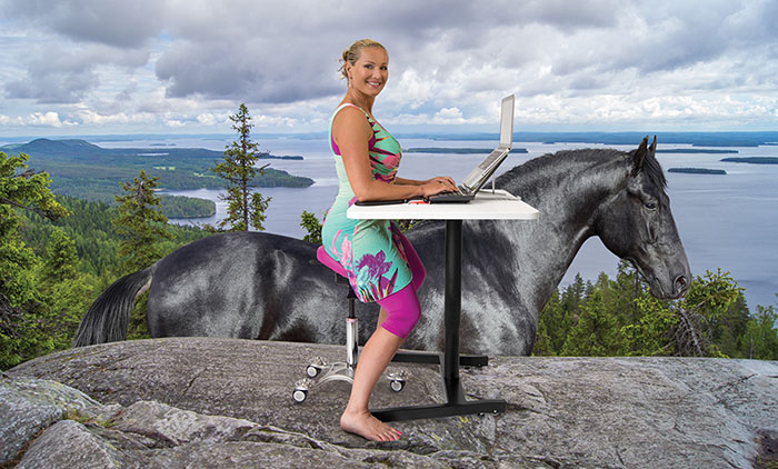 Nainen istuu kalliolla satulatuolilla pöydän ääressä, kuvaan editoitu hevonen, nainen näyttää istuvan myös hevosen selässä
